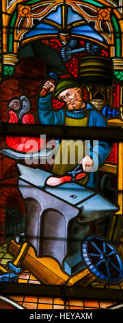 Glasmalerei-Fenster mit einem Schmied bei der Arbeit, in der Kathedrale St. Bavo in Gent, Flandern, Belgien. Stockfoto