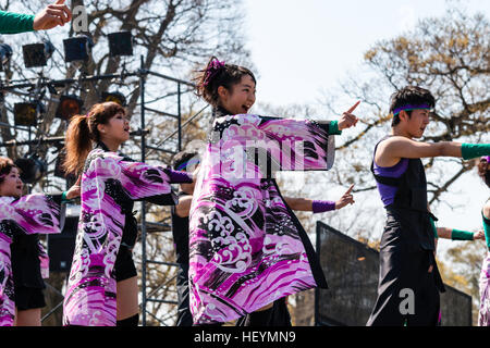 Japanische Yosakoi Festival. Junge lächelnde Tänzer, Männer und Frauen, stehen mit ausgestreckten Armen zeigen. Lila und Schwarz yukata Jacken tragen. Stockfoto