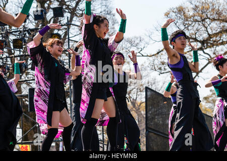 Japanische Yosakoi Festival. Dance Team auf der Bühne in erster Linie schwarze Kostüm, Tanzen und Singen, die Arme über dem Kopf angehoben. Im Freien, tagsüber. Stockfoto