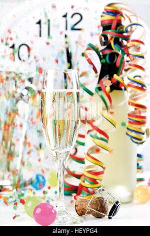 Glas und eine Flasche Champagner mit Luftschlangen und Konfetti, zeigt kurz vor 12:00 Uhr Stockfoto
