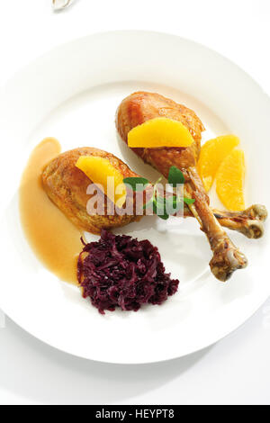 Gebratene Hähnchenschenkel oder Drumsticks garniert mit zwei orangefarbenen Segmente, Rotkohl, grüne Blätter und Soße Stockfoto