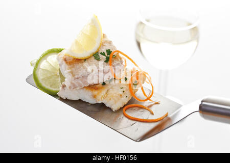 Fischgericht: spined Loach Filet, Zitronenscheibe und fein geschnittene Karotten auf einem Spatel, Glas Weißwein Stockfoto