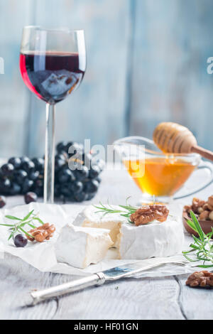 Brie Käse und eine Scheibe auf einem Holzbrett mit Nüssen, Honig und Rosmarin. Stockfoto