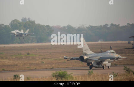 FA - 18D Hornet Flugzeug hebt ab, wie eine Thai f-16 wartet vom Flügel ein Royal Thai Air Force Base, Nakhon Ratchasima, Königreich von Thailand, 19 Februar während der Übung Cobra Gold 2014 abheben. CG 14 ist eine gemeinsame, multinationalen Übung im Königreich von Thailand zur Verbesserung und Erhöhung der multinationalen Interoperabilität jährlich durchgeführt. Die FA - 18D Hornet ist mit Marine alle Wetter Fighter Attack Squadron 242, Marine Aircraft Group 12, 1st Marine Aircraft Wing, III. Marine Expeditionary Force. Die f-16 ist mit Squadron 103, One Wing, Royal Thai Air Force. (U.S. Marine Corps Foto von Cpl. Ja Stockfoto