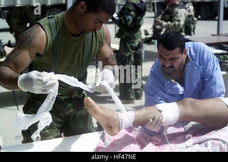 Ein uns Navy (USN) Hospital Corpsman zugewiesen, die 15. Marine Expeditionary Unit (MEU), helfen, ein zivilen irakischen Arzt mit Bereitstellung medizinischer Hilfe, eines irakischen Zivilisten verletzt während der Kämpfe zwischen Aufständischen und Koalition in der Nähe von Umm Qasr, Irak, während der Operation IRAQI FREEDOM zwingt. Iraqicasualty2003 Stockfoto