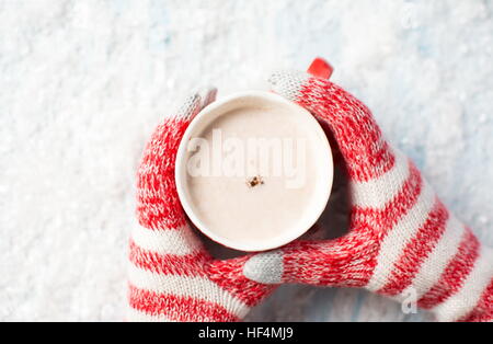 Weibliche Hände in Handschuhen Holding heiße Schokolade über einen Verschneiten Hintergrund Stockfoto