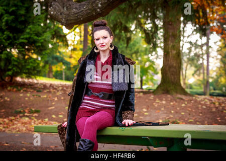Attraktive junge Frau in modischen Outfit, sitzt auf einem Picknick-Tisch im Park. Stockfoto