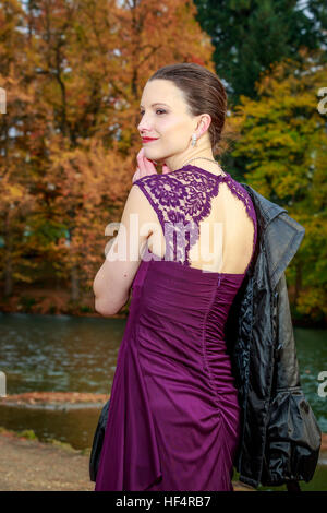 Attraktive junge Frau in modischen Outfit steht vor bunten Bäumen am Ufer. Stockfoto