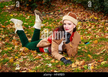 Attraktive junge Frau in modischen Outfit über gefallene Blätter Rollen. Stockfoto