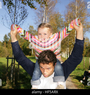 Vater geben seine drei-jährige Tochter eine Huckepack Fahrt Stockfoto