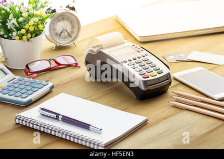 Kreditkarten-Terminal oder EDC auf Kasse Holztisch im Store mit Kreditkarte, Stift, Laptop und Gläser auf Hintergrund. Stockfoto