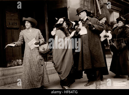 Suffragetten auf einem Stadt-Bürgersteig Wahlrecht Handzettel austeilen, um Passanten auf der Straße. Elizabeth T. Kent spricht nicht identifizierter Mann in Mantel und Bowler-Hut, Betrieb Napoléon, Center. Ca. Januar 1913. Stockfoto