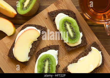 Vollkorn Brot Brötchen mit Frischkäse und frischen Apfel oder Kiwi Scheiben serviert mit Tee, mit Tageslicht fotografiert Stockfoto