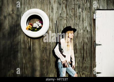 Frau mit Waffe gelehnt eine Holzwand mit weißen Reifen mit Blumen. Stockfoto