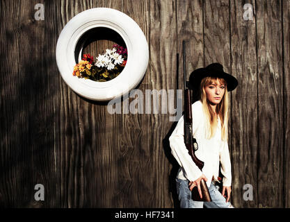 Frau mit Waffe gelehnt eine Holzwand mit weißen Reifen mit Blumen. Stockfoto