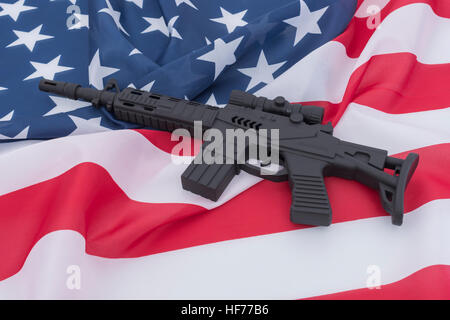 Schwarzes Spielzeug Sturmgewehr gegen US / amerikanische Flagge / Stars & Stripes gesetzt. Für US-Waffengewalt, US-Waffenrecht, Terrorismus, Chicago-Verbrechen, Arsenal Stockfoto