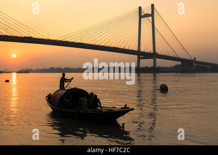 Hölzerne Land Boot am Fluss Hooghly bei Sonnenuntergang mit Vidyasagar Brücke vor dem Hintergrund (Silhouette). Stockfoto