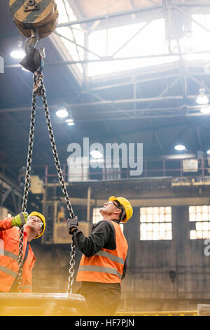 Stahlarbeiter blickte zu Kran-Kette in Fabrik Stockfoto