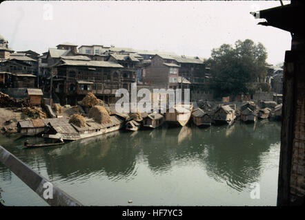 Ein Foto, das Häuser und Hausboote entlang des Jhelum River in Srinagar, Kaschmir, Indien zeigt. Das Bild zeigt den unverwechselbaren architektonischen Stil der Region und die ruhige Umgebung am Fluss. Stockfoto
