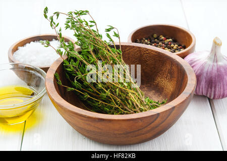 Gewürz-Zutaten: Thymian, Salz, Pfeffer, Chili, Knoblauch, Olivenöl in Schalen auf weißem rustikalen Holztisch Stockfoto