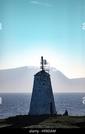 Twr Bach Beacon silhouetted gegen die untergehende Sonne mit Blick aufs Meer Nebel rollwing in über das Meer in Richtung Küstengebirge auf der Llyn Halbinsel, Anglesy, Wales, Großbritannien Stockfoto