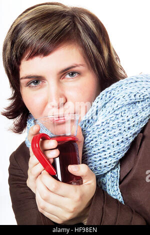 Junge Frau eingewickelt in einen Schal, eine Tasse Tee hält, hat sie eine Erkältung Stockfoto