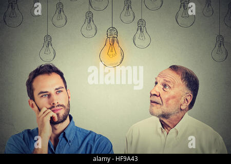 Kognitiven Fähigkeiten Konzept, Alter Mann Vs junger Mensch. Senior Woman und junge Kerl helle Glühbirne auf graue Wand Hintergrund isoliert betrachten Stockfoto
