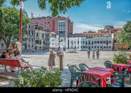 Sommer in Venedig, Italien. Älteres Paar und Touristen Ruhe im Baum Schatten auf dem Platz. Eine Menge von Freundschaft und liebevolle Gesten Stockfoto