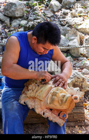 Mann Hand Schnitzen einer traditionellen Maya-Szenenverlaufs aus Holz zu verkaufen an seinem Stand auf dem Gelände von Chichén Itzá Tempel Yucatan, Mexiko Stockfoto