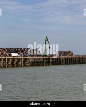 Schrottplatz voller zerquetschten Autos und der Kran mit einer Klaue, die sie in einen riesigen Haufen bewegt. Am Wasser in Newhaven. Stockfoto