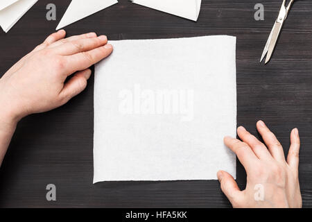 Draufsicht der Hände halten leeres Blatt Papier vor dem zusammenklappen um herauszufinden auf dunklen braunen Holztisch zu machen Stockfoto