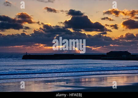 Sonnenuntergang über Porthcawl Ufermauer und Licht Haus. Blau und Orange Wolken express die kalte Herbstluft mit den Strahlen der Sonne die Wolken piercing Stockfoto