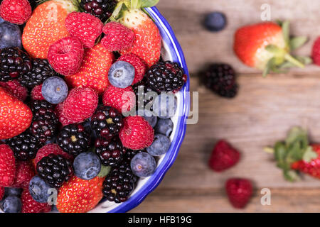 Draufsicht auf eine Schüssel mit Sommerfrüchten, bestehend aus Erdbeeren, Himbeeren, Heidelbeeren und Brombeeren, über eine alte Holz Hintergrund. Stockfoto