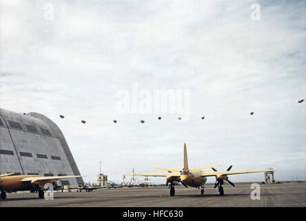 Martin JM-1 Marauder und North American SNJ Texan parken um 1944 in der Nähe des Hauptluftschiffes Hangar. JM-1 wurden als Zielschlepper verwendet. Neun L-Typ-Blimps fliegen in der Ferne in einer Linienformation und demonstrieren die Ausbildung der US Navy und die Luftkoordination während des Zweiten Weltkriegs Stockfoto