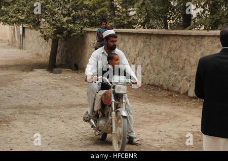 Ein afghanischer Mann und sein Sohn sitzen auf einem Motorrad in der Nähe ein Schlüssel-Leader Engagement zwischen Provincial Reconstruction Team (PRT) Farah Ärzte, afghanische Ärzte und öffentliche Gesundheit Profis am städtischen Krankenhaus Farah, Okt. 30.  PRT Farah-Mission ist zu trainieren, beraten und helfen afghanischen Staats-und Regierungschefs bei den Stadtwerken, Bezirk und Landesebene in Farah Provinz Afghanistans. Ihre zivile Militär-Team besteht aus Mitgliedern der US Navy, US Army, U.S. Department of State und der US Agency for International Development (USAID).  (U.S. Navy Photo von Lt. j.g. Matthew Stroup/rel Stockfoto