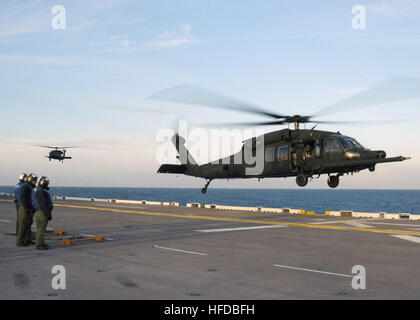 US Navy (USN) Luft-Abteilung Matrosen, Wasp-Klasse amphibischen Angriff Schiff, USS BATAAN (LHD-5), Stand-by mit Unterlegkeile und Ketten als zwei Hubschrauber der US Army (USA) UH - 60M Black Hawk (Blackhawk), 160. Special Operations Aviation Regiment (SOAR), Fort Campbell, Kentucky (KY), bereiten Sie an Bord landen im Cockpit als Bestandteil ihrer über Wasser Qualifizierungsprogramm. Zwei UH - 60M, 160. SOAR auf USS Bataan am 10. Februar 2006 Stockfoto