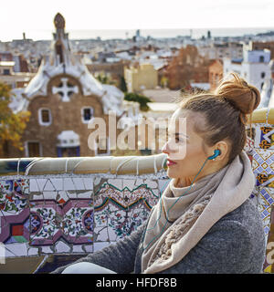 Barcelona-Handschrift. moderne Reisende Frau im Mantel im Park Güell in Barcelona, Spanien hören Audioguide auf Bank sitzend Stockfoto