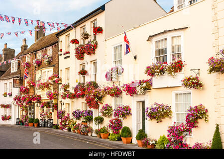 England, beschäftigen. Blick entlang der Zeile des 17. und 18. Jahrhundert Gebäude entlang der Strandpromenade, alle mit roten Blüten in den Feldern geschmückt. Malerisch. Sunlit. Union Jack. Stockfoto