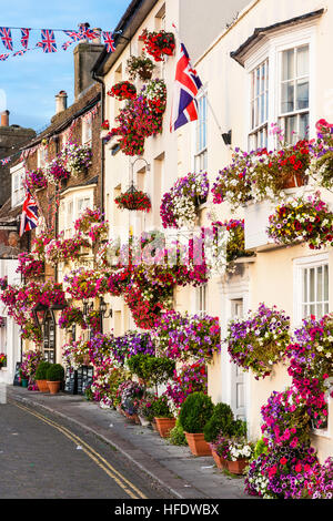 England, beschäftigen. Blick entlang der Zeile des 17. und 18. Jahrhundert Gebäude entlang der Strandpromenade, alle mit roten Blüten in den Feldern geschmückt. Malerisch. Sunlit. Union Jack. Stockfoto