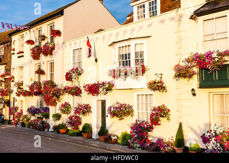 England, beschäftigen. Blick entlang der Zeile des 17. und 18. Jahrhundert Gebäude entlang der Strandpromenade, alle mit roten Blüten in den Feldern geschmückt. Malerisch. Sunlit. Union Jack. Stockfoto