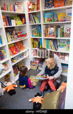 Eine Mutter, ein Waliser Sprache Buch zu lesen, zu ihren Kindern in Siop y Pethe, kleine unabhängige Waliser Sprache Buchhandlung und Geschenk shop, Aberystwyth Wales UK - Interieur Stockfoto