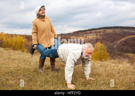 Älteres Ehepaar mit Spaß und spielen die Schubkarre in der Natur.  "Frau trug seinen Mann bis ins hohe Alter." Stockfoto