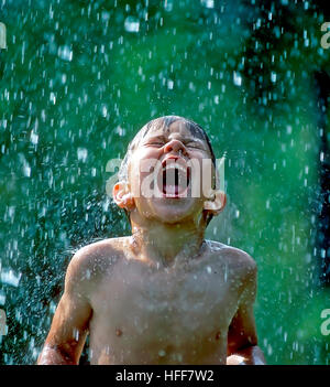 Ein kleiner Junge fängt Regentropfen in den offenen Mund mit einem Ausdruck von purer Lebensfreude und jugendlichem Übermut. Stockfoto