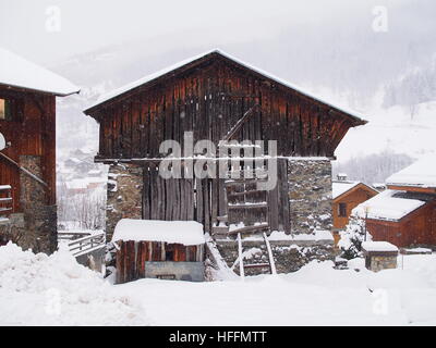 Alte Holzhütte sitzt im fallenden Schnee und steht im Kontrast zum nebeligen Hintergrund des Berges Stockfoto