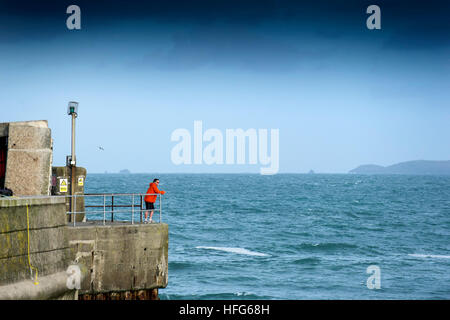 Ein Mann steht am Kai mit Blick auf den Eingang zum Hafen von Newquay in Cornwall. Stockfoto