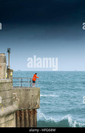 Ein Mann steht am Kai mit Blick auf den Eingang zum Hafen von Newquay in Cornwall, England, UK. Stockfoto