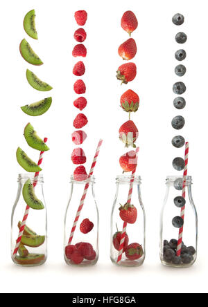 Beerenfrüchte und Kiwi fallen in Glasflaschen mit einem Strohhalm über einen weißen Hintergrund Stockfoto