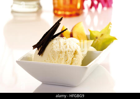 Schüssel mit Vanilleeis garniert mit Schokolade Späne, Mango Scheiben und Sternfrüchte Stockfoto