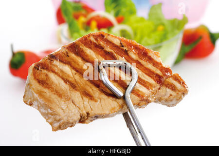 Grill Zange halten gegrilltes Schweinekotelett, Grill Marken, Schüssel Salat im Hintergrund Stockfoto