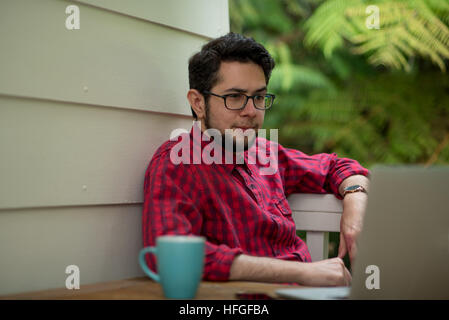Junger Mann mit Laptop und Smartphone zu Hause im Freien sitzen Stockfoto